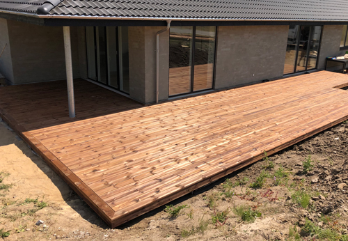 L-shaped wooden deck build around the corner of the house. It has a solid foundation made with GroundPlug® TwisterTM foundations.